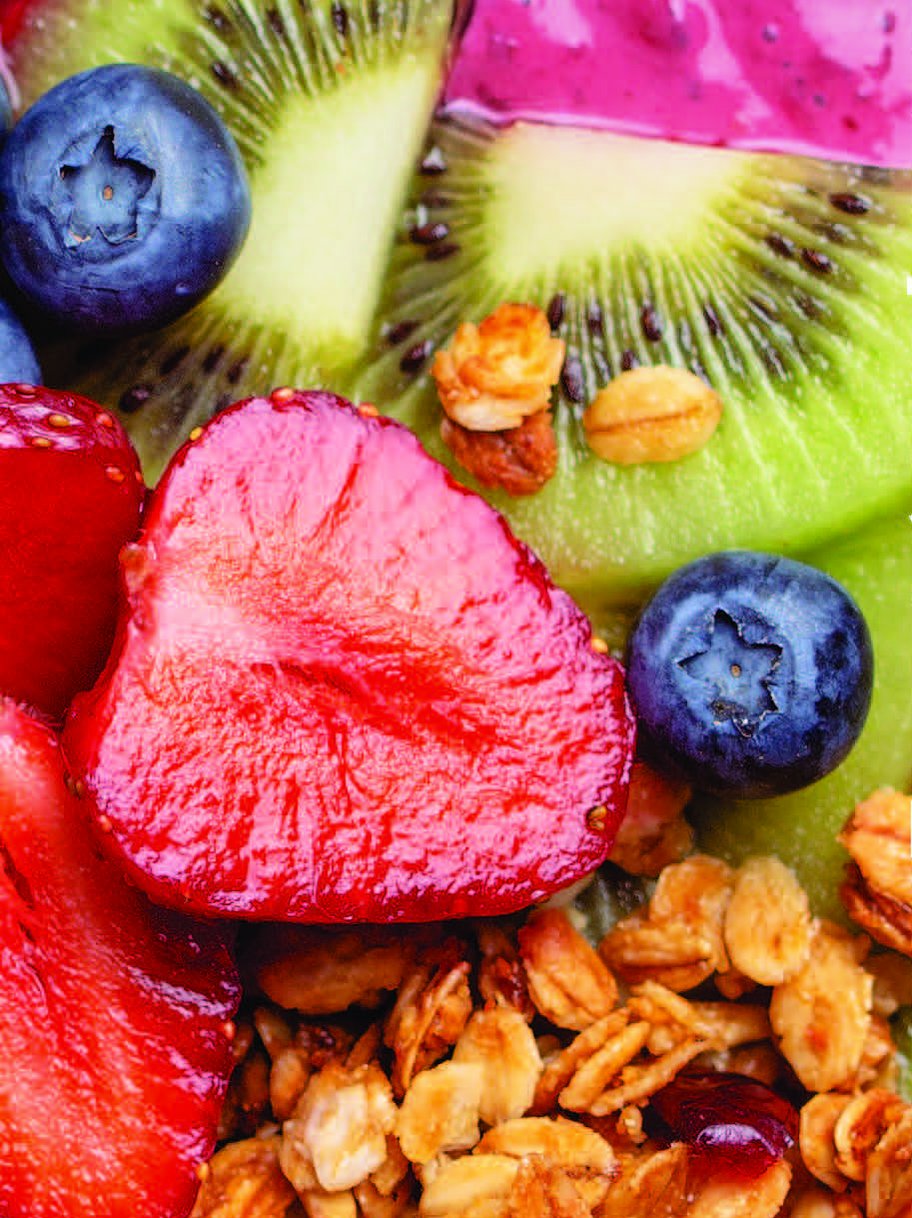 Eine Smoothie-Bowl mit Müsli, Erdbeeren, Kiwi und Blaubeeren auf einem rosa Hintergrund, mit deutschem Text überlagert.