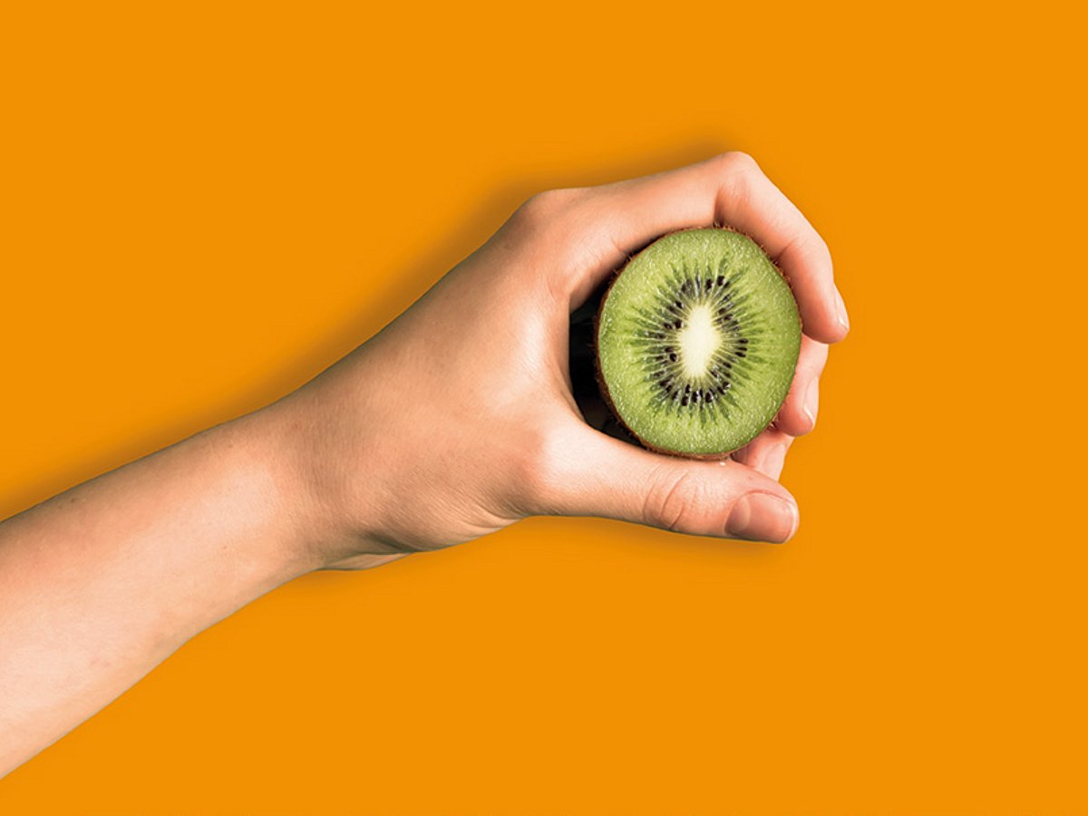 Eine Hand hält eine halbe Kiwi vor einem orangefarbenen Hintergrund mit deutschem Text über Einsparungen bei der Krankenversicherung.