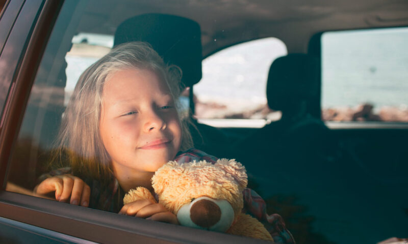 Kind mit Teddybär schaut aus dem Autofenster