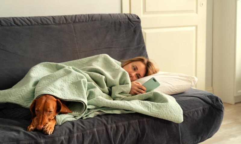 Frau liegt mit ihrem Hund antriebslos auf dem Sofa.