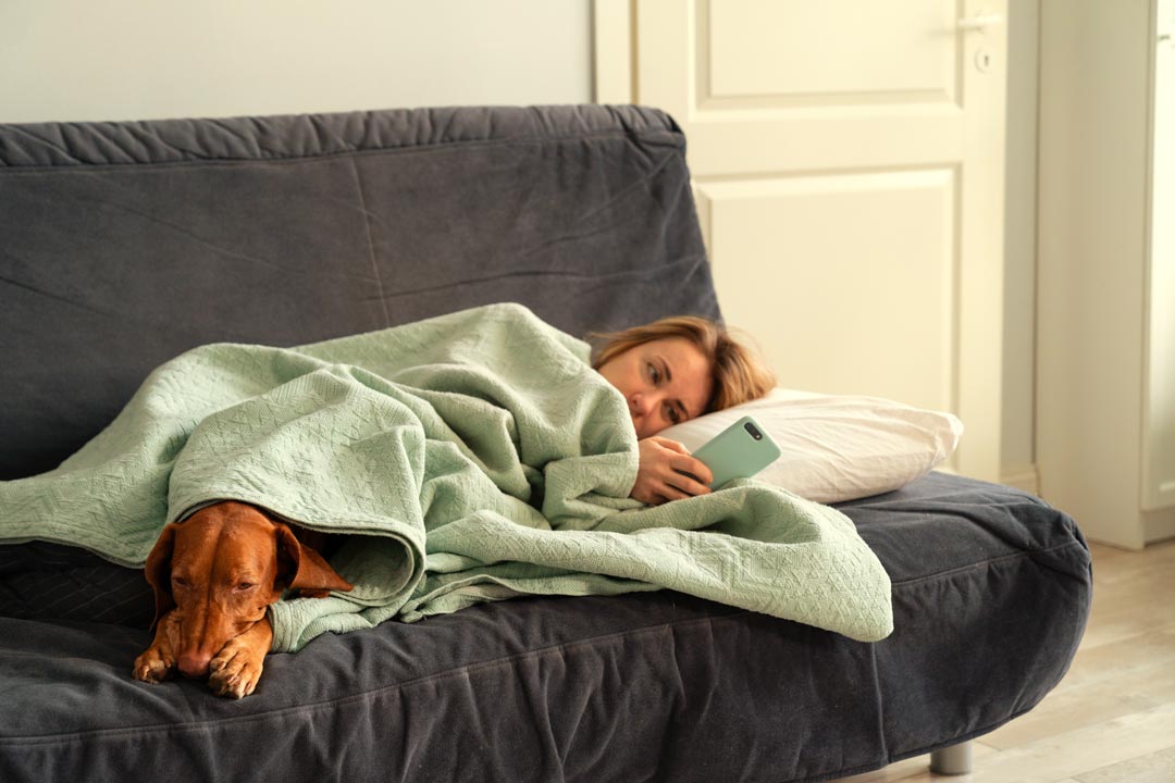 Frau liegt mit ihrem Hund antriebslos auf dem Sofa.