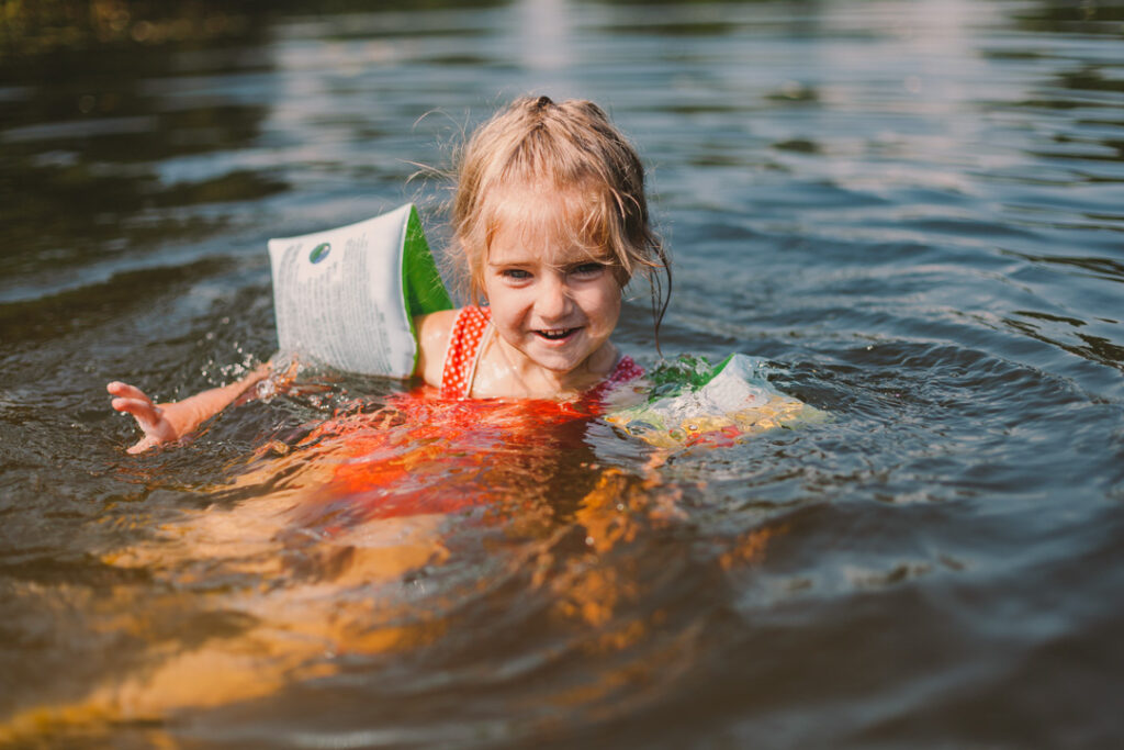 Kleines Mädchen mit Schwimmflügeln schwimmt im See.