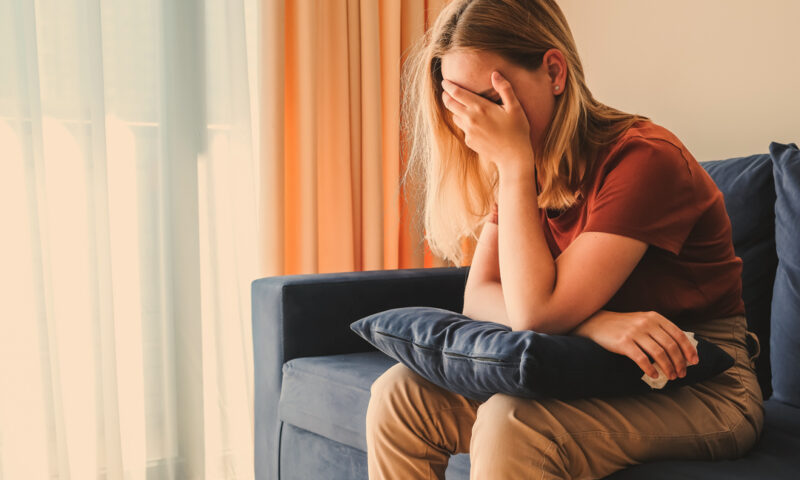 eine frau sitzt auf dem sofa und fasst sich an den kopf