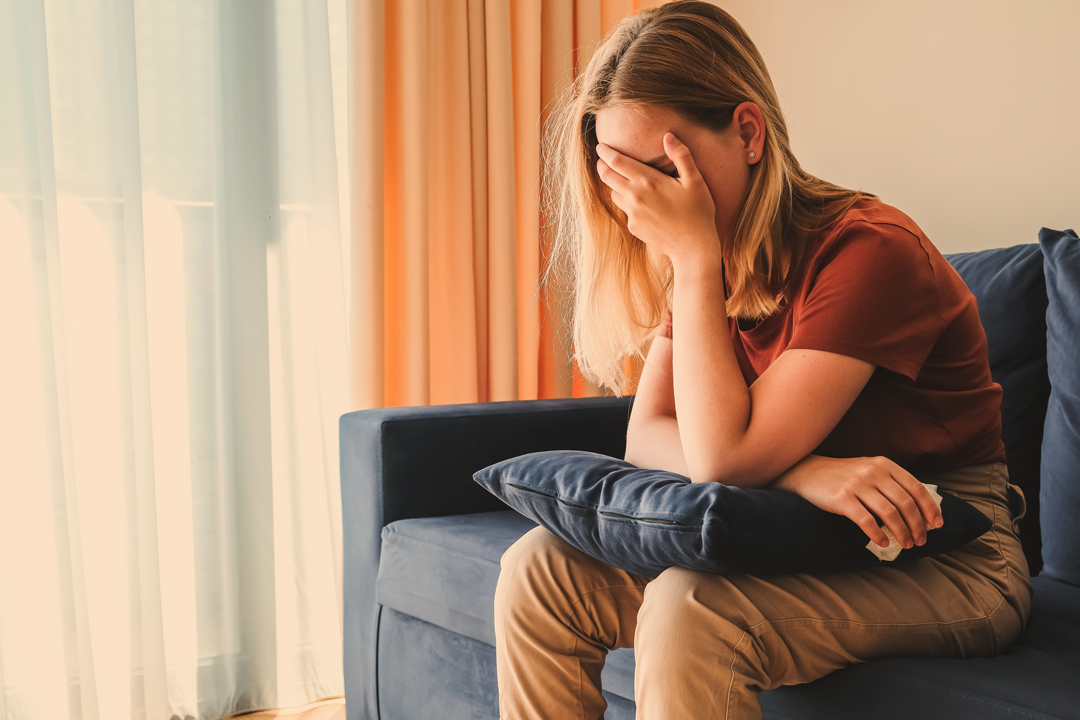 eine frau sitzt auf dem sofa und fasst sich an den kopf